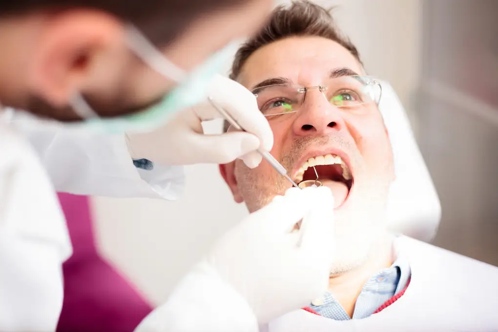 Mid adult man having his teeth examined by a young male dentist in dental clinic. High angle close-up view