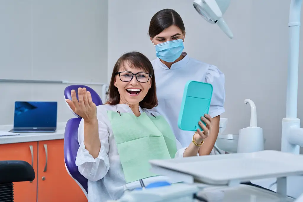 Woman patient together with dentist, patient sitting in dental chair looking at mirror